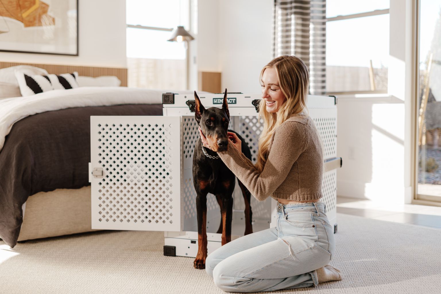 Crate train adult dog: woman sitting with a Doberman next to its crate